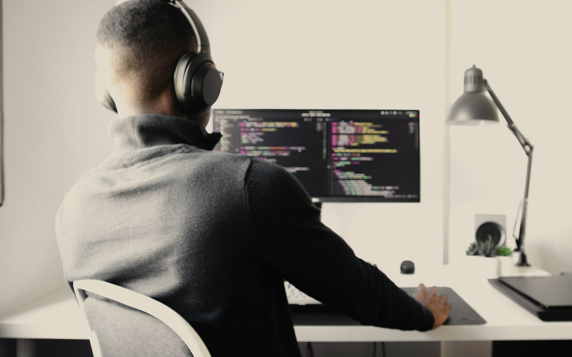 A developer wearing headphones works on code at a monitor in a bright room